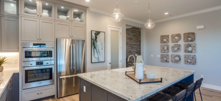 A sleek kitchen with stainless steel double ovens, a built-in refrigerator, a large kitchen island with quartz countertops, and glass-front cabinets above the appliances.