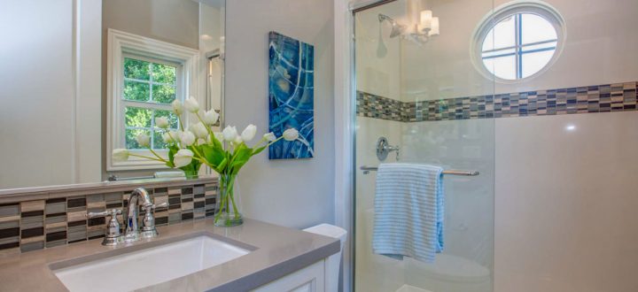 A modern bathroom featuring a glass-enclosed shower, a vanity with white cabinetry, and a floral decoration on the counter.