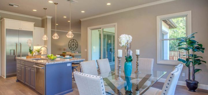 An open kitchen and dining area with modern lighting, a large island, and a dining table with upholstered chairs in neutral tones.