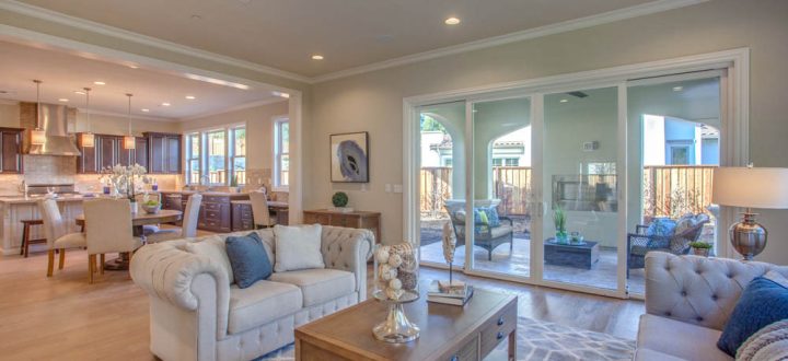 A well-appointed living room with a beige color scheme, featuring plush sofas, a patterned area rug, and an open layout that leads to a dining area and kitchen.
