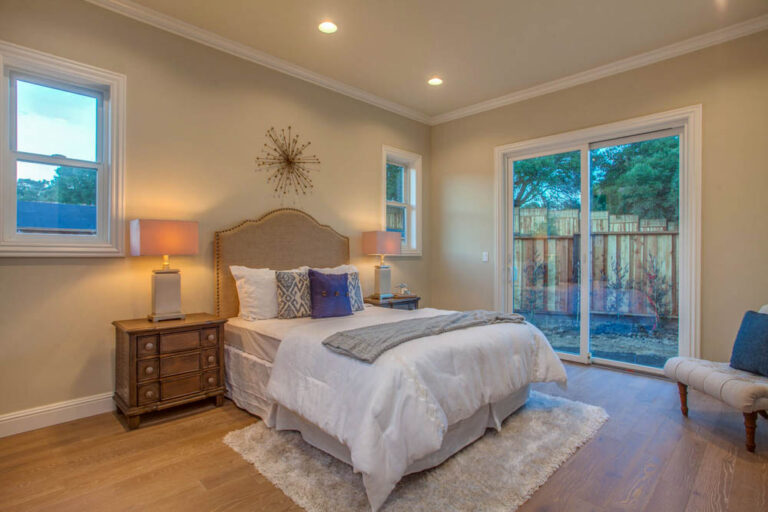 A comfortable bedroom featuring a queen-sized bed with decorative pillows, a large window, and sliding glass doors leading to an outside area.
