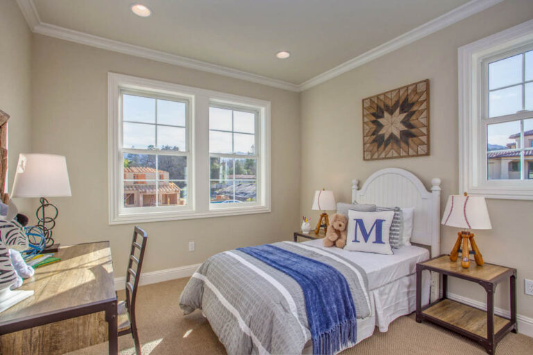 A well-lit bedroom tailored for a young resident, featuring a single bed, playful decorations, and ample natural light from large windows.