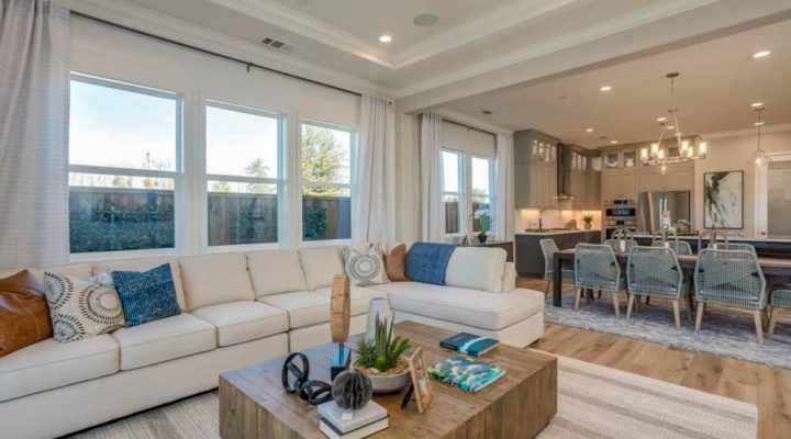 Luxurious open-plan living room featuring a large white sectional sofa, coastal-themed decor, and an attached dining area with modern chairs and pendant lighting, showing a seamless transition for stylish living.