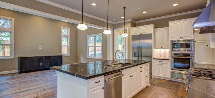 Contemporary kitchen showcasing dual tone cabinets, a central island with a sink, and modern appliances, all under elegant pendant lighting, designed for functionality and style.