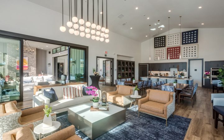 A contemporary living space with a mix of seating options, including sofas and armchairs, arranged around a coffee table. The room is adorned with abstract artwork on the walls and large windows that allow natural light to enhance the ambiance.