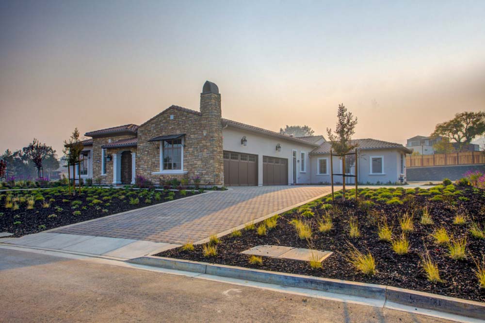 Luxurious stone-front home featuring a meticulous landscape with various plants and a spacious driveway, showcasing grand architecture and modern living.