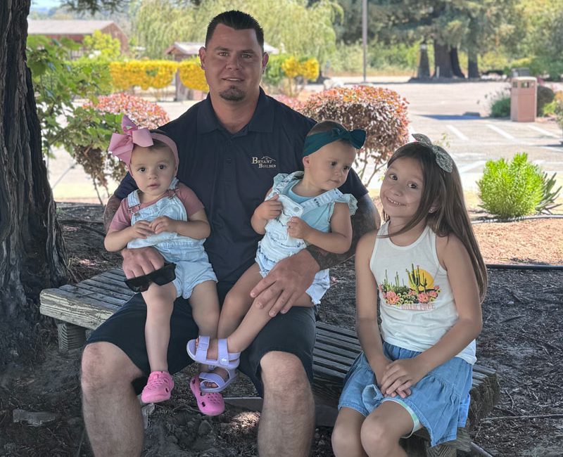 The owner of Bryant Builders seated outdoors with his three young children, showing a warm family moment.