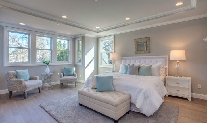 A luxurious bedroom with a seating area by the windows, featuring light-colored furniture and a soft, relaxing ambiance.