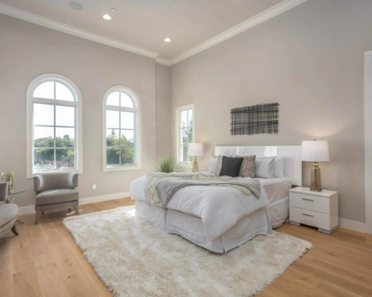 Tranquil master bedroom with natural light, featuring a large bed with white bedding, two large arched windows, and a plush area rug, offering a peaceful retreat designed with comfort and style in mind.