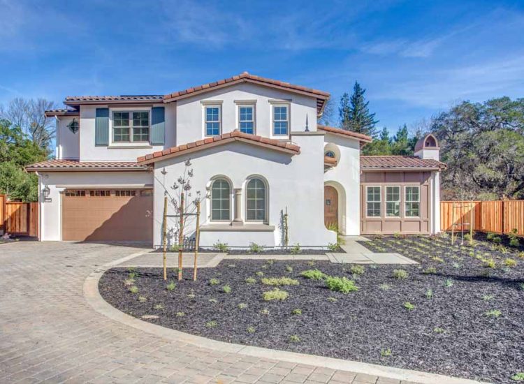 A Mediterranean-style two-story home with white walls, a tiled roof, arched windows, and a spacious driveway.