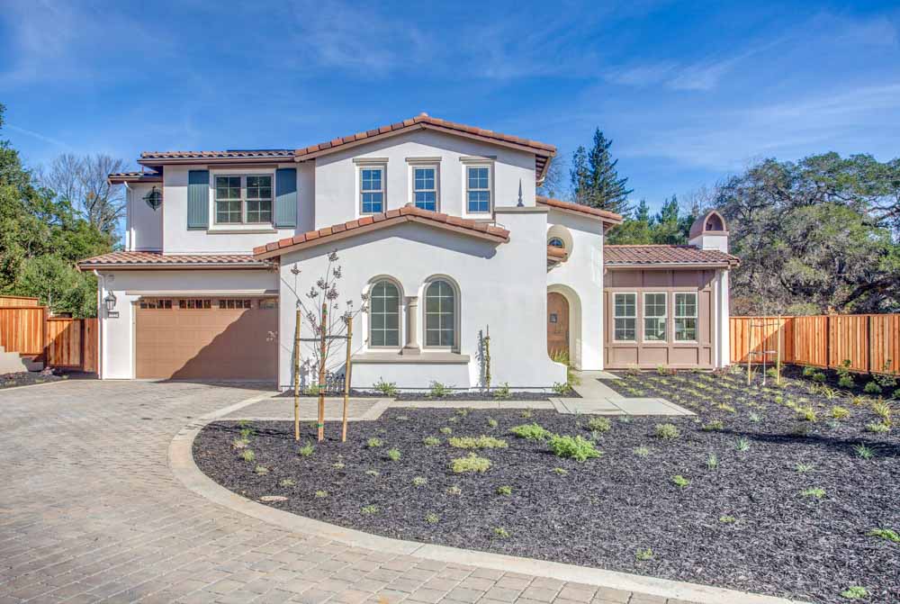A Mediterranean-style two-story home with white walls, a tiled roof, arched windows, and a spacious driveway.