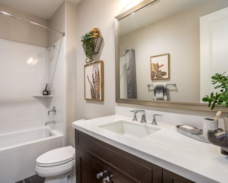 A bright, modern bathroom featuring a sleek white vanity, wall-mounted art, and green accents, with a shower-tub combo on the left.