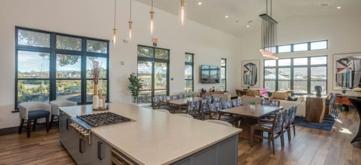 A large kitchen and dining area in a modern clubhouse, featuring a kitchen island and long dining tables for gatherings.