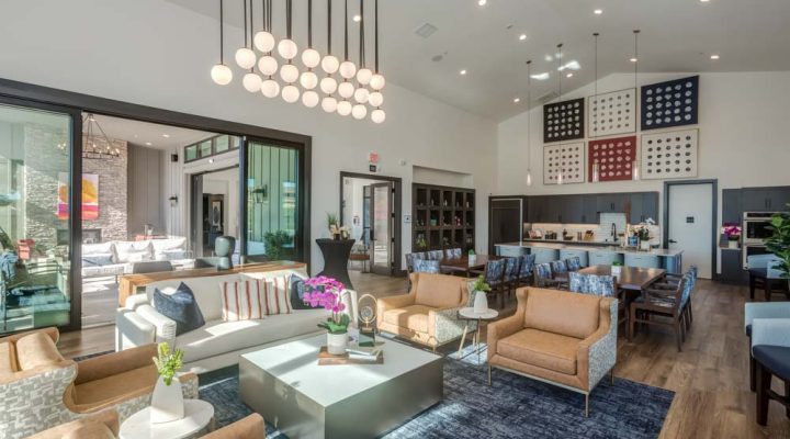 A well-lit clubhouse featuring modern lounge seating, contemporary decor, and a spacious kitchen area in the background.