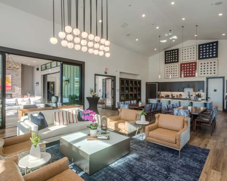 A well-lit clubhouse featuring modern lounge seating, contemporary decor, and a spacious kitchen area in the background.