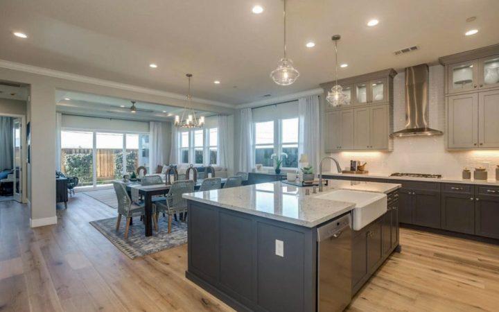 Elegant and spacious modern kitchen with gray cabinetry, marble countertops, and a large central island featuring a farmhouse sink and stylish pendant lights, designed for both functionality and aesthetic appeal.