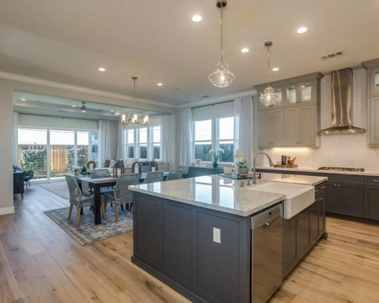 Elegant and spacious modern kitchen with gray cabinetry, marble countertops, and a large central island featuring a farmhouse sink and stylish pendant lights, designed for both functionality and aesthetic appeal.