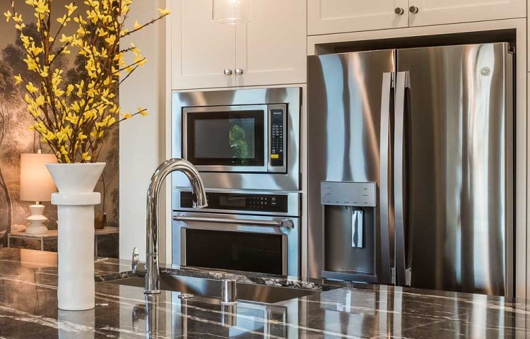 A close-up view of modern stainless steel kitchen appliances, including a refrigerator, microwave, and oven, paired with a sleek marble countertop and stylish decor.