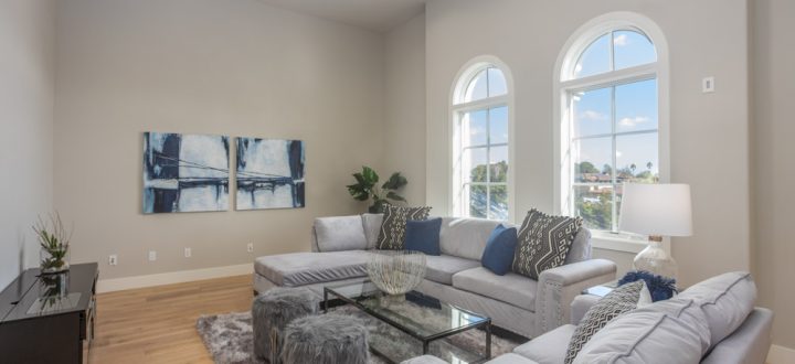 Stylish living room featuring plush gray sofas, arched windows providing abundant natural light, and modern decor accents including a glass coffee table and a large blue abstract painting.