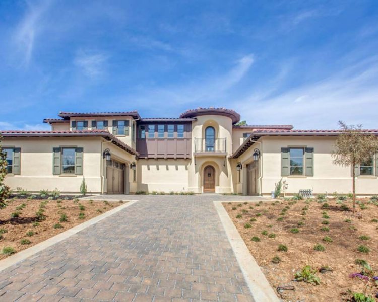Modern villa with beige stucco exterior, tile roof, and paved driveway, showcasing stylish architectural design.