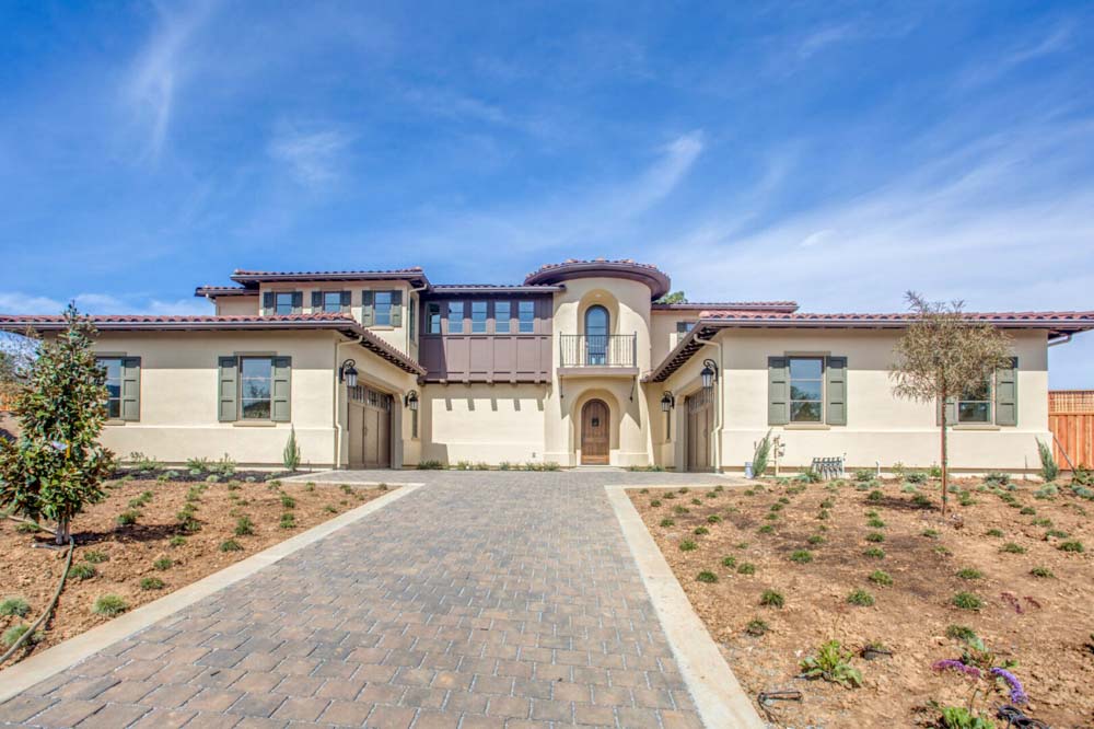Modern villa with beige stucco exterior, tile roof, and paved driveway, showcasing stylish architectural design.