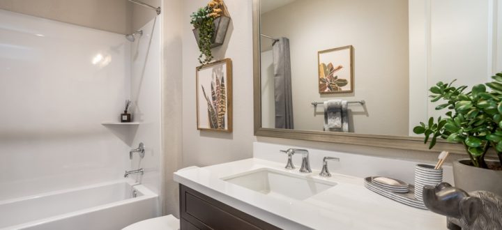 A bright, modern bathroom featuring a sleek white vanity, wall-mounted art, and green accents, with a shower-tub combo on the left.