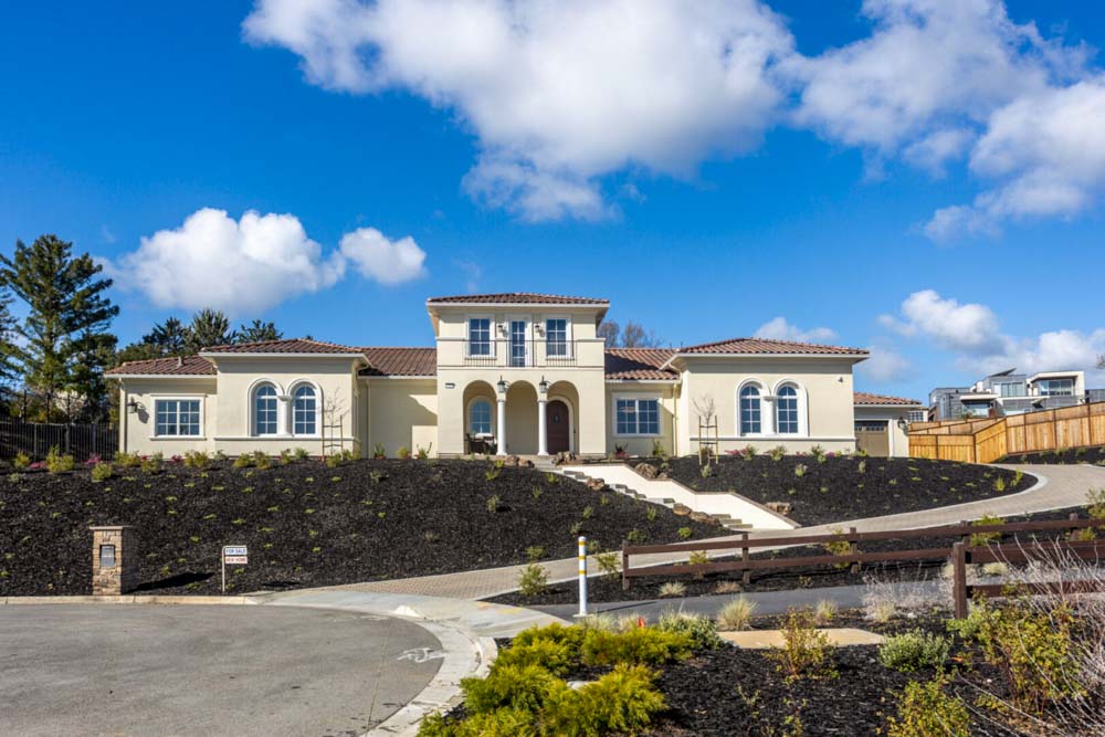 Newly constructed home featuring a large driveway and scenic landscaping under a clear blue sky.