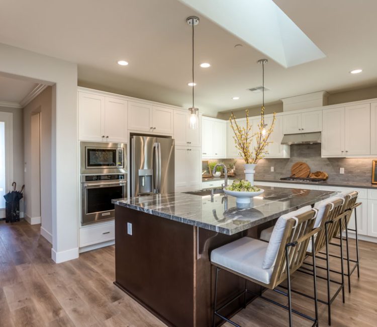 A bright and open kitchen featuring a large marble island, stainless steel appliances, and modern pendant lighting.