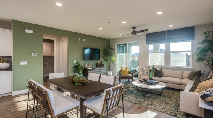 A bright and open living room and dining area with green accent walls, a comfortable seating arrangement, and large windows bringing in ample natural light, perfect for family gatherings.