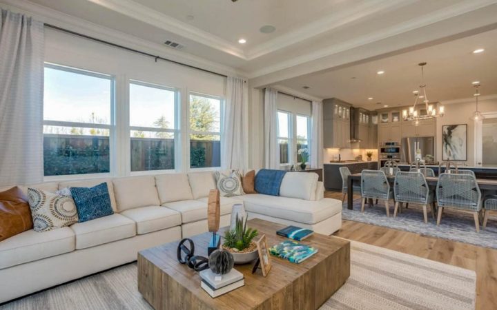 Luxurious open-plan living room featuring a large white sectional sofa, coastal-themed decor, and an attached dining area with modern chairs and pendant lighting, showing a seamless transition for stylish living.