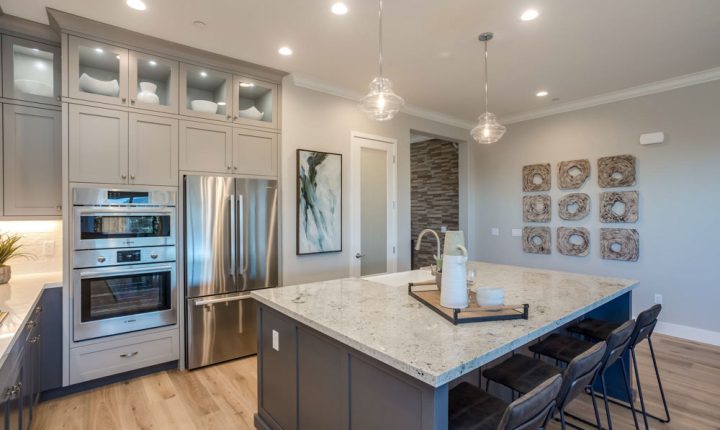 A sleek kitchen with stainless steel double ovens, a built-in refrigerator, a large kitchen island with quartz countertops, and glass-front cabinets above the appliances.