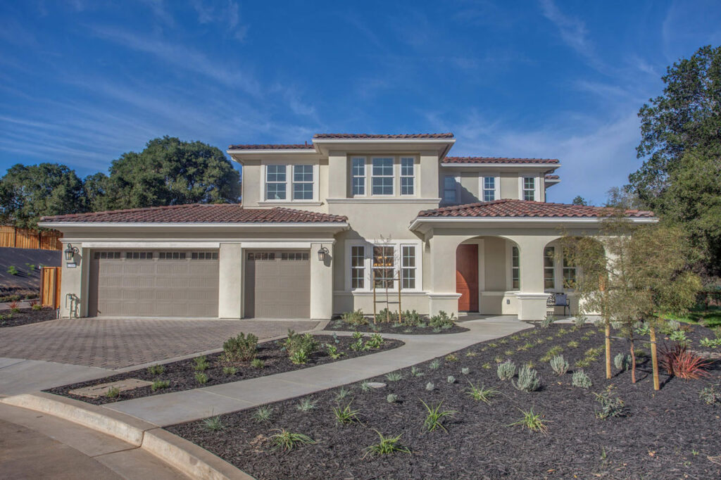 A front exterior view of a modern two-story home with Spanish architectural elements, a beige facade, and a welcoming arched entryway.