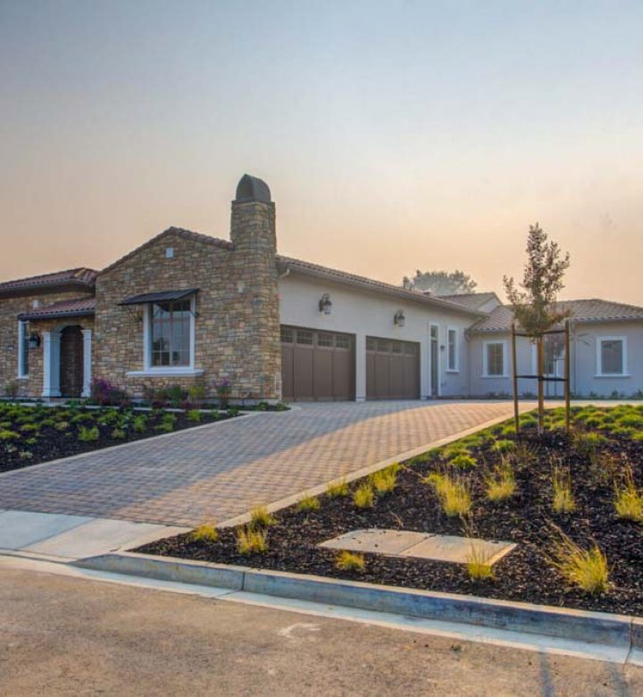 Luxurious stone-front home featuring a meticulous landscape with various plants and a spacious driveway, showcasing grand architecture and modern living.