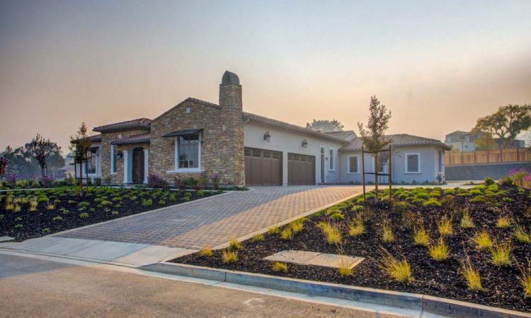 Luxurious stone-front home featuring a meticulous landscape with various plants and a spacious driveway, showcasing grand architecture and modern living.