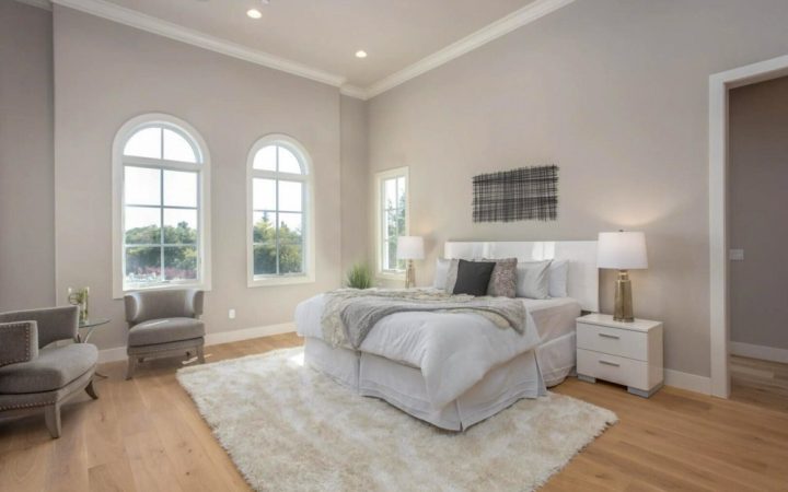 Tranquil master bedroom with natural light, featuring a large bed with white bedding, two large arched windows, and a plush area rug, offering a peaceful retreat designed with comfort and style in mind.